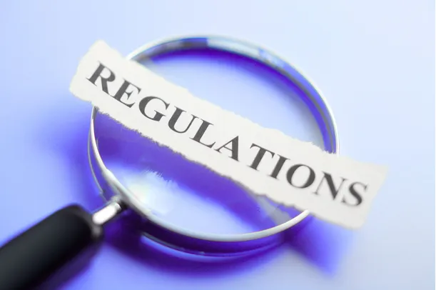 A magnifying glass focused on a torn paper reading REGULATIONS — the global regulatory landscape this session maps